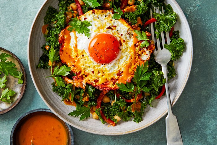 Turmeric-fried-eggs-and-kale-salad Plate of kale salad topped with a turmeric fried eggnext to a ramekin of dressing and parsley