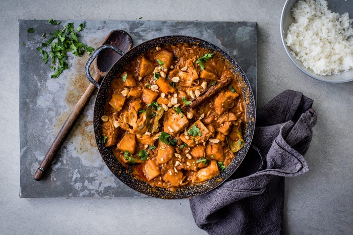 Vegan Jackfruit Curry Recipe Skillet of vegan jackfruit curry next to a wooden spoon and tea towel