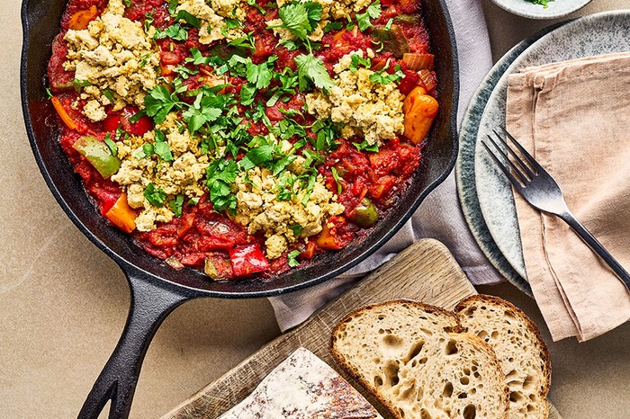 Vegan shakshuka Vegan shakshuka topped with fresh parsley next to a board of bread and bowl of parsley and two plates with a tea towel