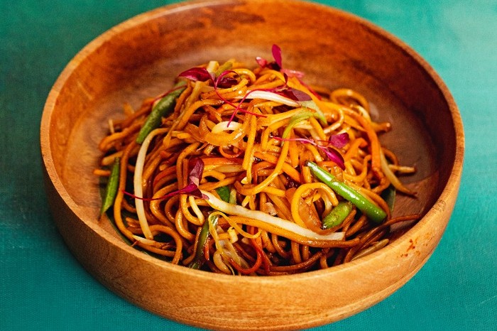 Vegetable hakka noodles A wooden bowl filled with noodles and veg on a green background