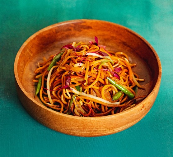 Vegetable hakka noodles A wooden bowl filled with noodles and veg on a green background