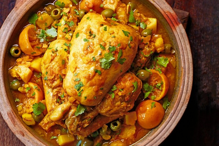 Whole braised chicken with lemon and olives Chicken in a pot surrounded by vegetables an topped with herbs